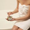 A woman in a bathrobe using the Invigorating Body Polish from The Retreat