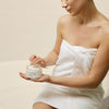 A woman in a bathrobe using Nourishing Body Butter from The Retreat