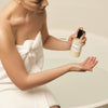 A woman in a bathrobe using the Purifying Cream Oil Body Wash from The Retreat